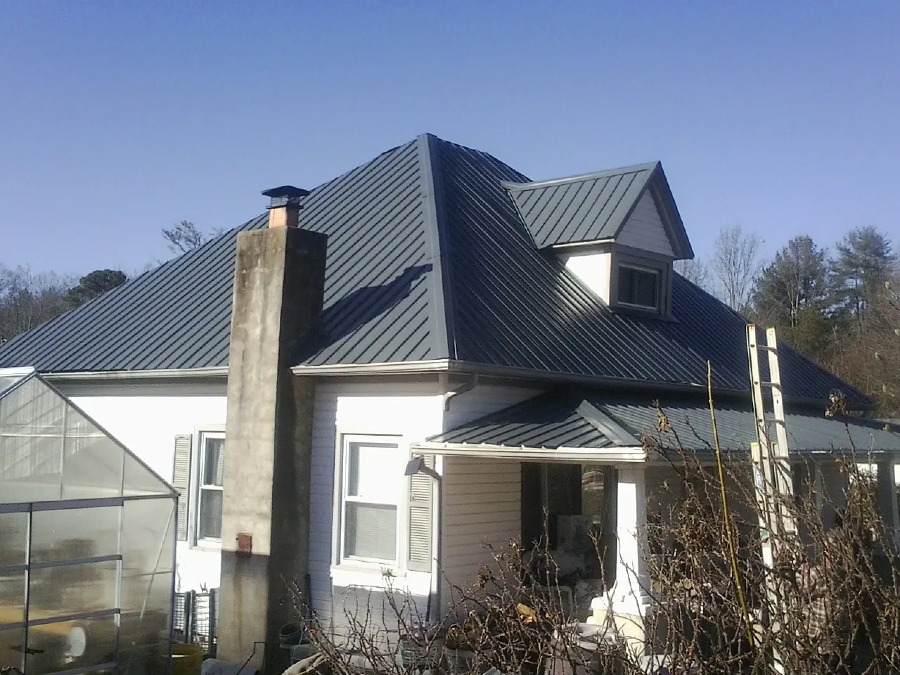 Dark blue standing seam metal roof on a white farmhouse with dormer — Slate & Tile Roof Repair by Roofing Brothers in Doniphan