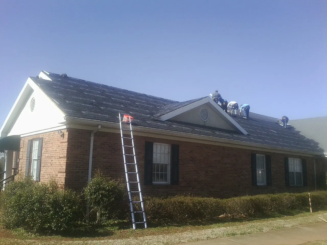 Crew tearing shingles off a brick ranch roof with a ladder set — Emergency Roof Repair work by our crew in Doniphan