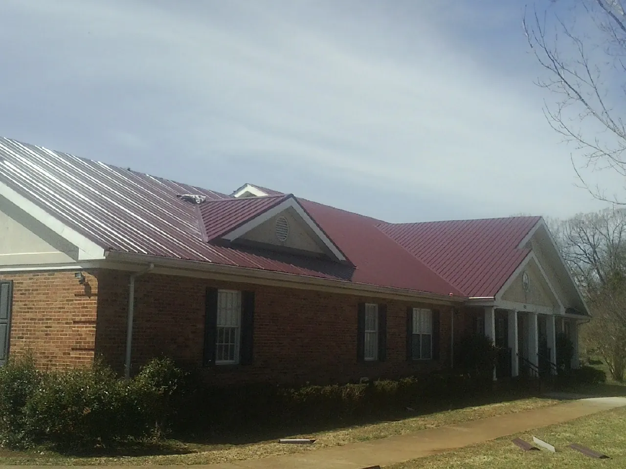 Red metal roof with gabled entries on a long brick building, from a Hail Damage Roof Repair job in Doniphan