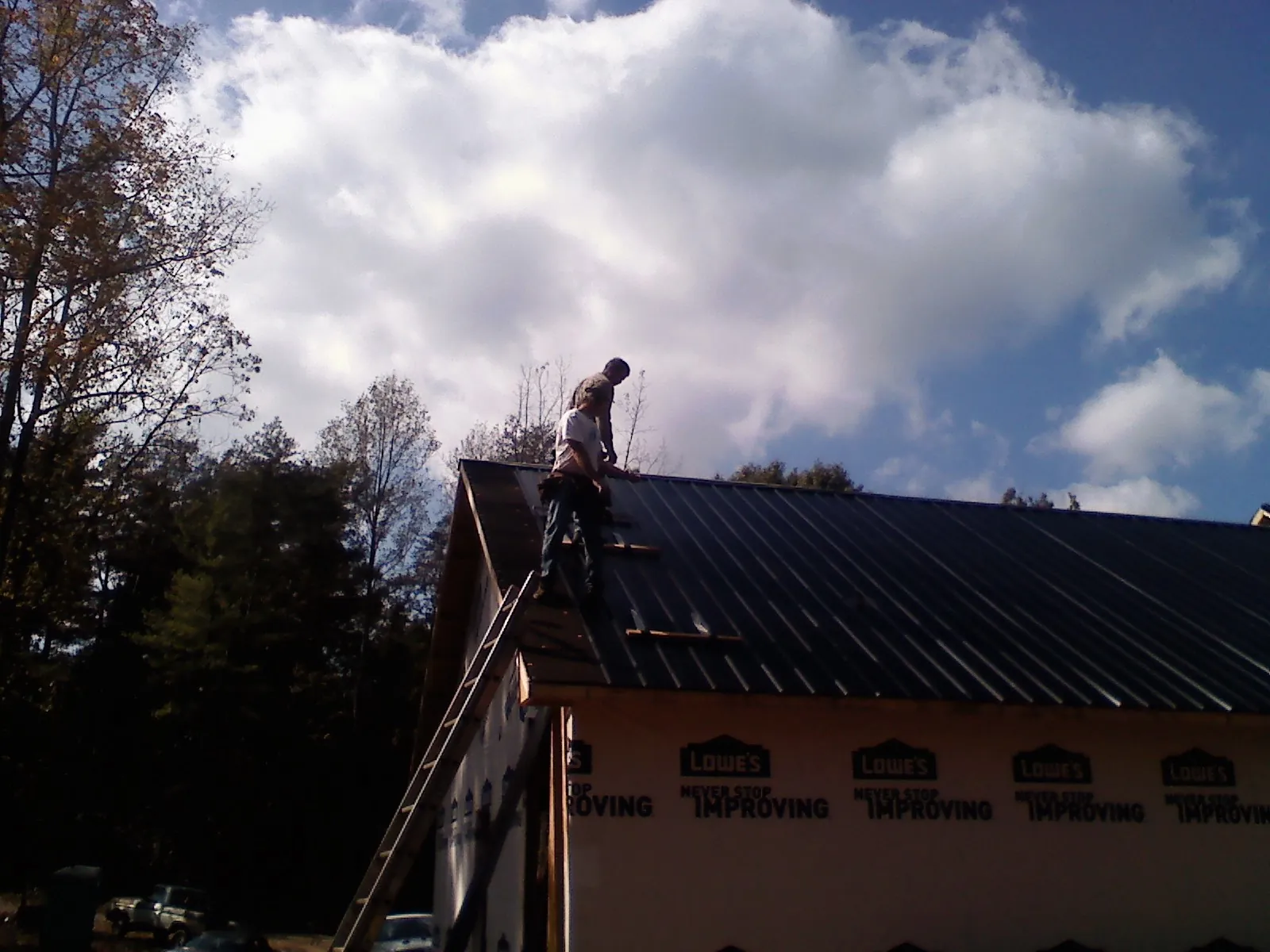 Roofer fastening dark metal panels high against a cloudy sky, from a Roof Inspection job in Doniphan