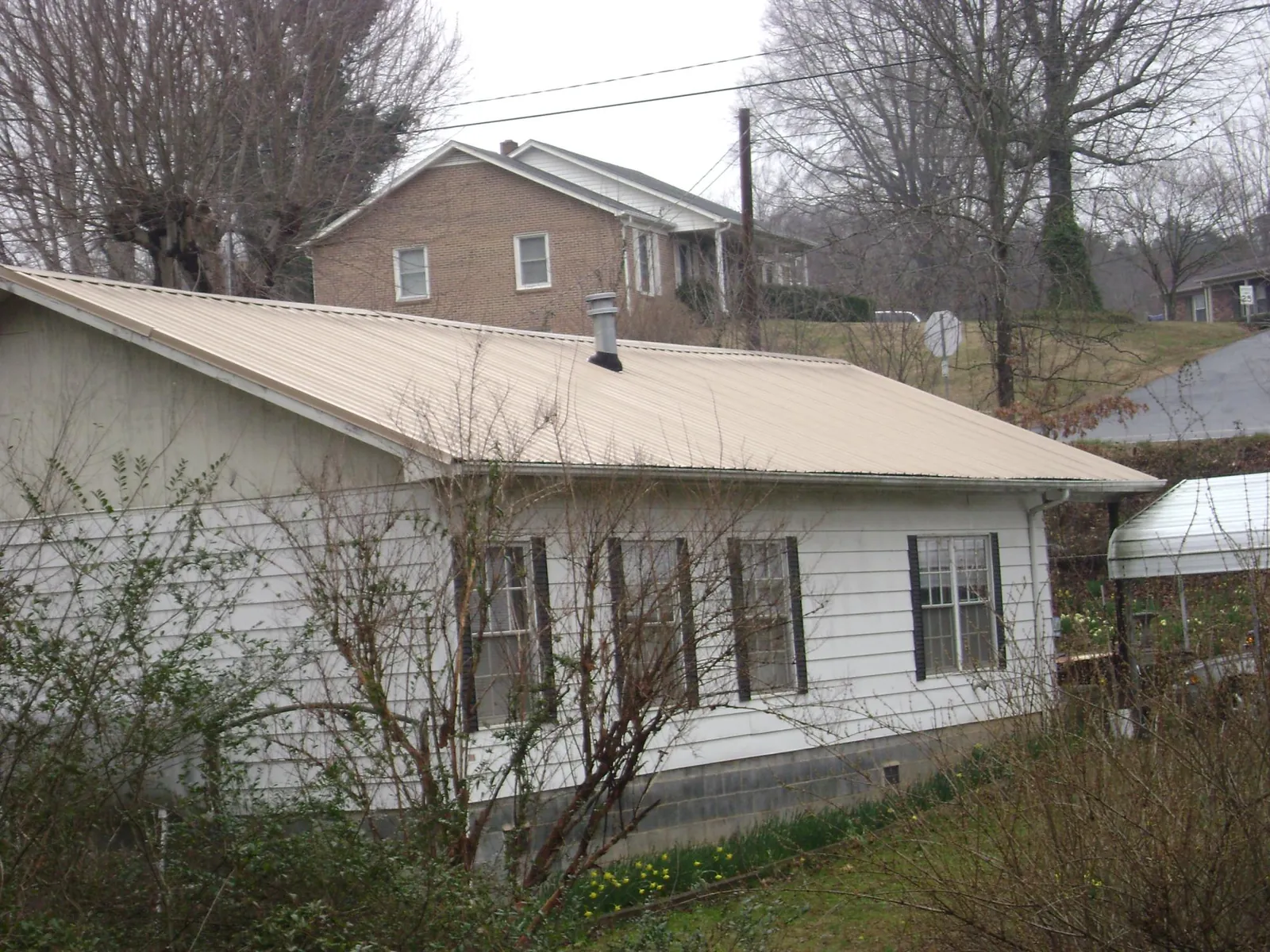 Tan metal roof on a white sided house set into a hillside — Commercial Roofing by Roofing Brothers in Doniphan