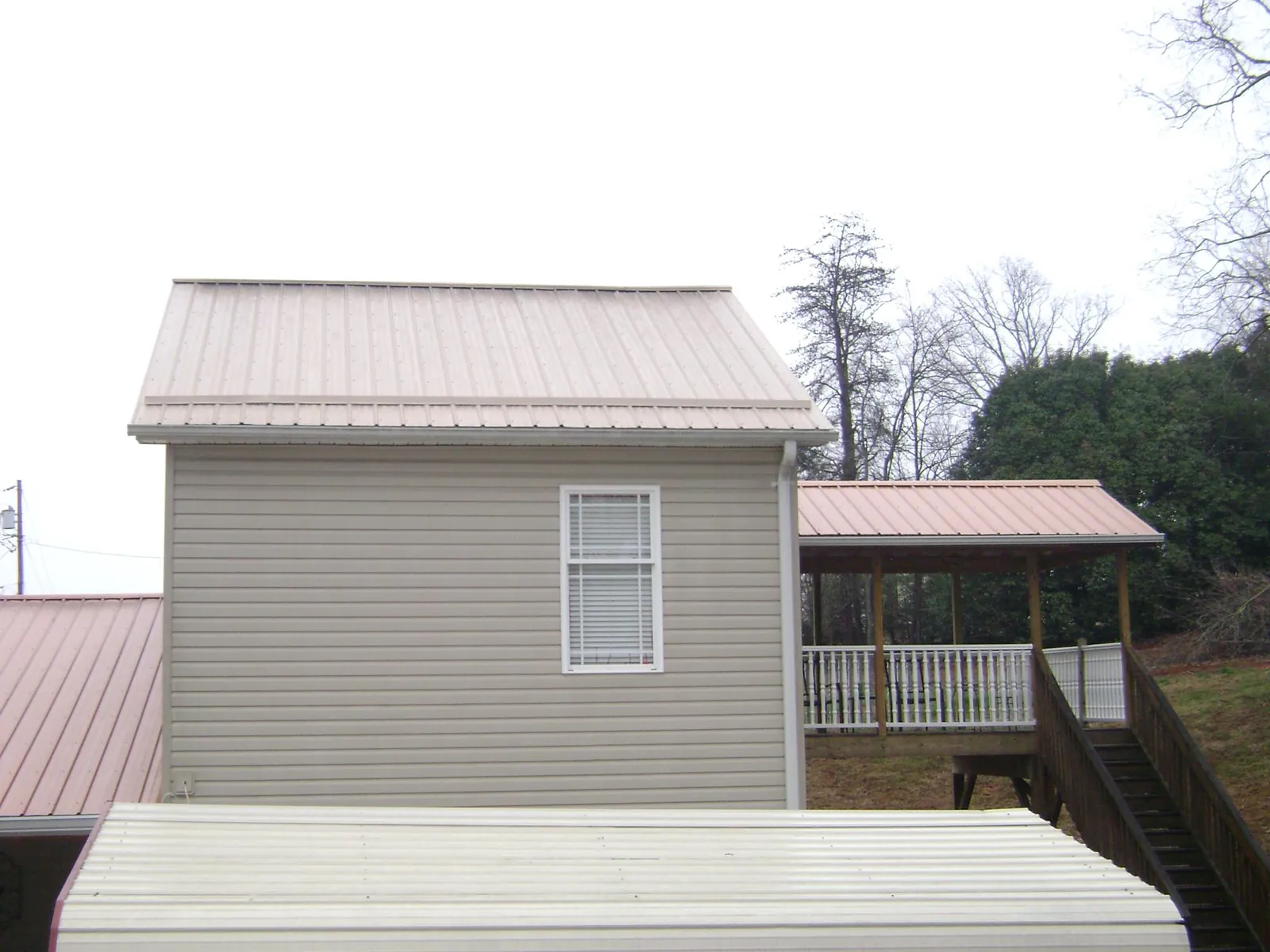 Tan metal roofs on a two story addition and attached porch, from a Roof Replacement job in Doniphan